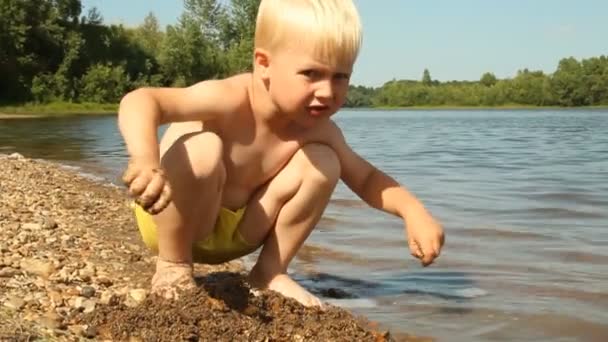 Um rapazinho a brincar na margem do lago. Recreação à água — Vídeo de Stock