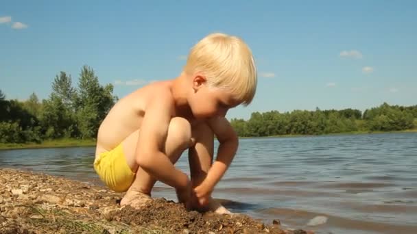 Маленький хлопчик грає на березі озера. Вода відпочинку — стокове відео