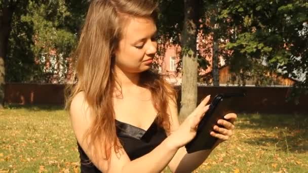 Una joven en un parque con una tableta. Verano — Vídeos de Stock