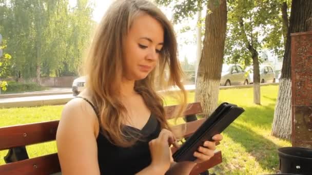 Ein junges Mädchen in einem Park mit einem Tablet-Computer. Sommer — Stockvideo