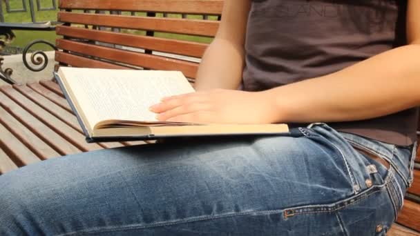 A young girl reading a book on a bench. Summer city park — Stock Video