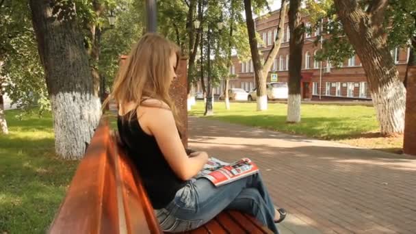 Jovem lendo uma revista brilhante no parque — Vídeo de Stock