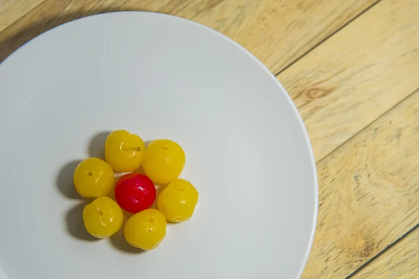 Red cherry in group of yellow cherry on white plate — Stock Photo, Image