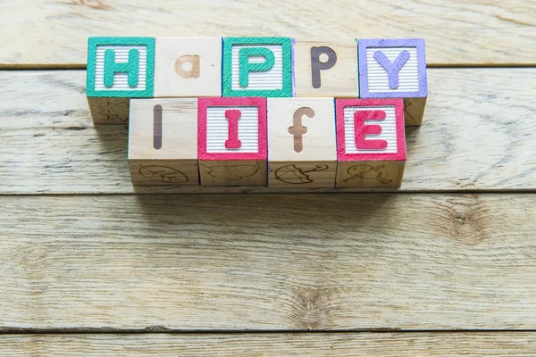 Dřevěný blok slovo je šťastný život na dřevěné pozadí — Stock fotografie