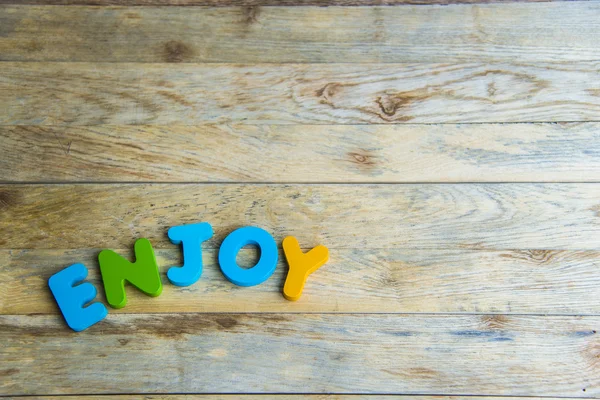 Colorful wooden word Enjoy on wooden floor — Stock Photo, Image