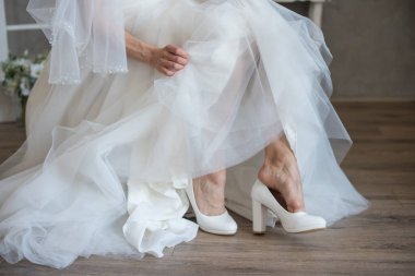 Gelin beyaz gelinlik içinde ayakkabı giyiyor. 