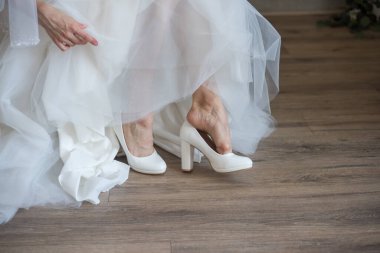 Gelin beyaz gelinlik içinde ayakkabı giyiyor. 