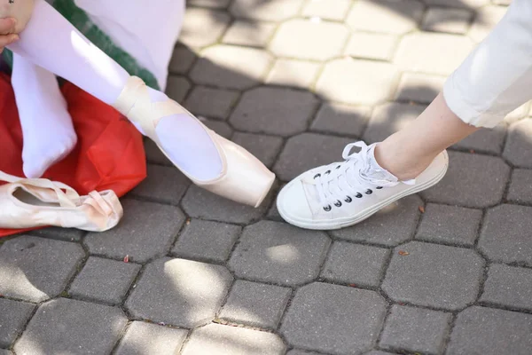 feet of ballerina wearing pointe shoes and woman in white sneakers on the street