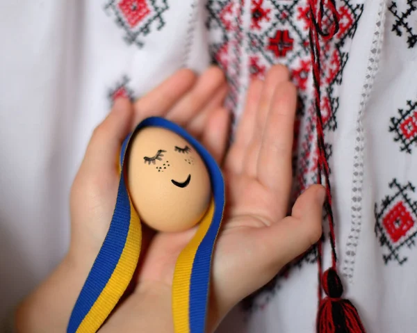 Yüzü boyalı yumurta, Ukrayna kurdelesi ve arka planda Ukrayna süsü. Paskalya arkaplanı.