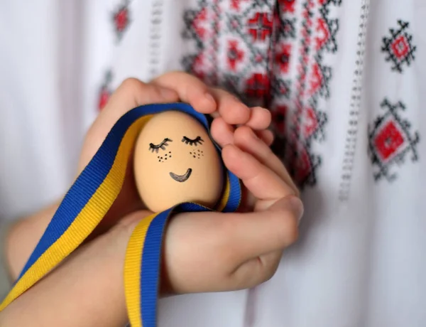 Yüzü boyalı yumurta, Ukrayna kurdelesi ve arka planda Ukrayna süsü. Paskalya arkaplanı.