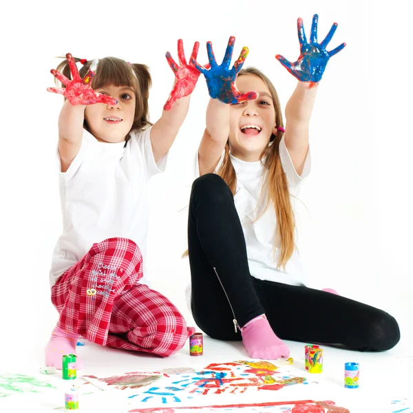 Två glada tjejer leker med finger färger på vit bakgrund Stockbild