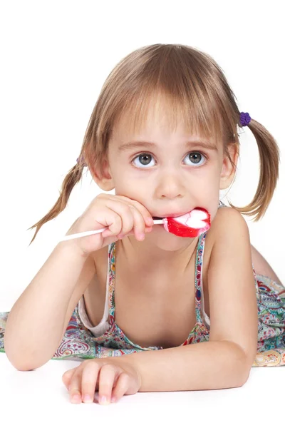 Little girl biting red heart-shaped lollipop — Stock Photo, Image