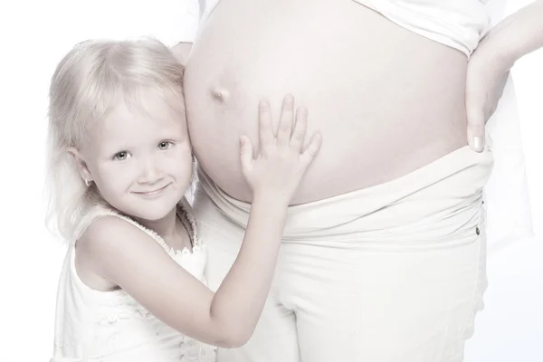 Милая улыбающаяся маленькая девочка слушает живот своей беременной матери — стоковое фото