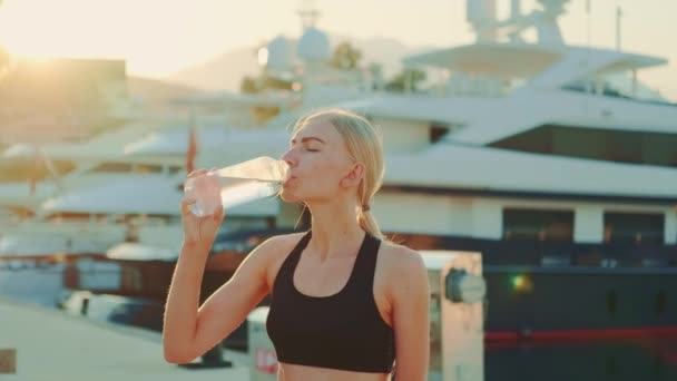 Zoom shot of fitness woman drinking water from bottle in sunny rays — Stock videók
