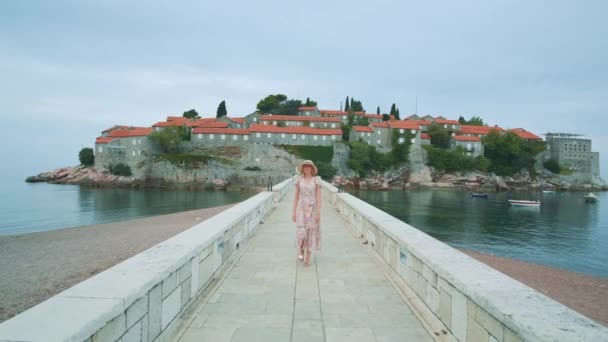 A long stone bridge with pretty woman walking from the island washed by the sea — Stockvideo