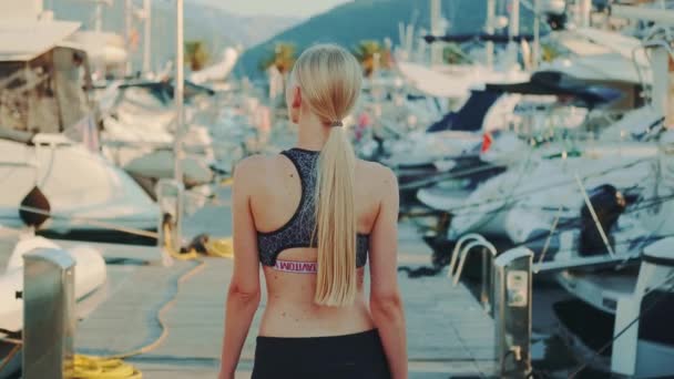 Back view of slim woman in gym outfit walking in yacht port — Stock Video