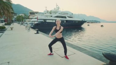 Siyah spor kıyafetli sarışın kadın şehir rıhtımında çömeliyor.