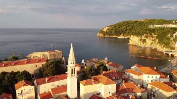 Über alte Gebäude mit roten Dächern und Kirchturm fliegen. Drohnenangriff auf Altstadt Budva in Montenegro. — Stockvideo