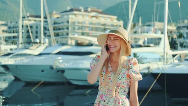 Елегантна жінка говорить по смартфону на вулиці з яхтами на задньому плані — стокове відео