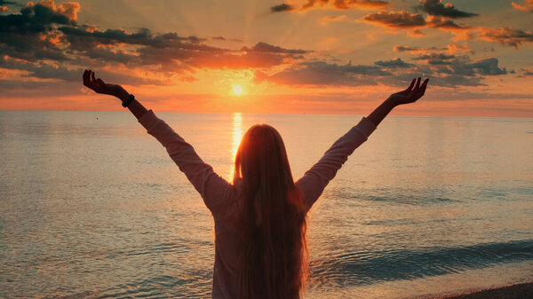 Young woman with outstretched arms enjoying the beauty of sunset on the sea
