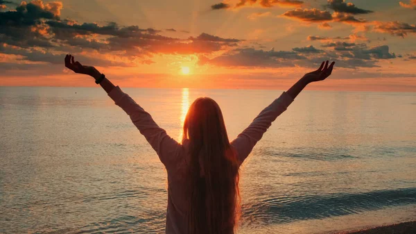 Молода жінка з простягнутими руками насолоджується красою заходу сонця на морі Стокове Зображення