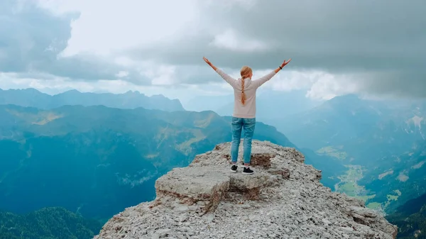 Молода жінка з простягнутими руками насолоджується красою природи на гірському скелі Стокове Зображення