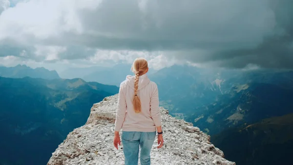 Back view of blonde woman walking on the top of the mountain under the clouds