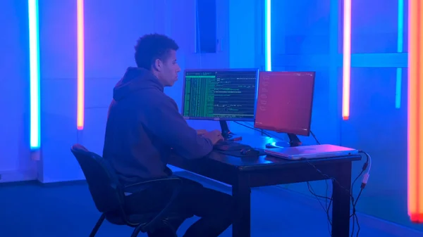 Młody Afrykanin pisze programy hakerskie w ciemnym pokoju ze światłami neonowymi — Zdjęcie stockowe