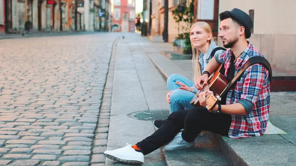 Mã e mulher sentados na calçada, tocando guitarra e descansando — Fotografia de Stock