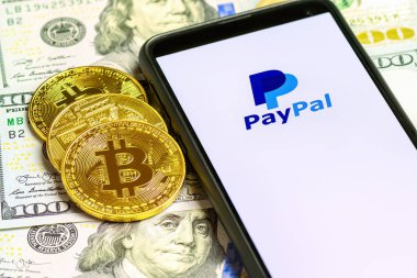 MOSCOW, RUSSIA - 14 Ekim 2021: Akıllı telefon ekranında PayPal logosu Bitcoin Cryptocurrency Coins ve ABD dolar banknotlarının arka planında. Paypal internet tabanlı dijital para aktarım servisidir.