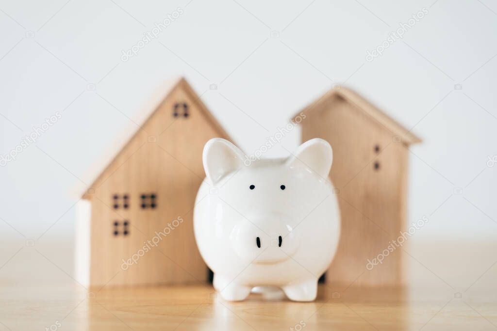 Wooden house with white piggy bank on wooden table. saving money for buying house, financial plan home loan concept.