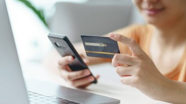 Kredi kartı tutan ve internet alışverişi, internet bankacılığı, e-ticaret için akıllı telefon kullanan genç bir kadın ev konseptinden para harcıyor.