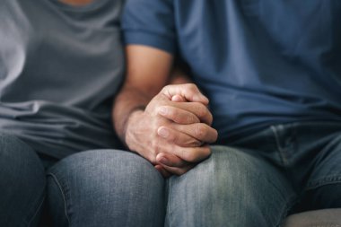 Kanepede oturan Asyalı olgun çifti yakından çek. Karı ve koca mutlu bir şekilde el ele tutuşuyorlar. Sevgi, güvenlik ve sigorta ailesi