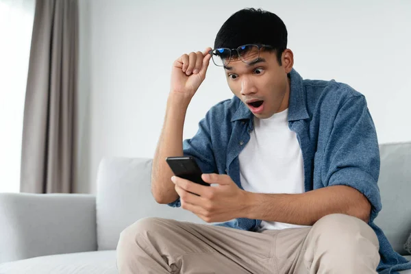 Portrait of excited asian man looking at mobile phone, man receiving good news using smartphone at home.