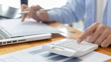 İşadamı, şirketin gelirlerini hesaplamak ve özel ofisindeki gelirleri, finans ve muhasebe bilgilerini, şirket performansını ve gelirlerini analiz etmek için hesap makinesine baskı yapıyor..