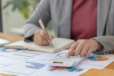 Muhasebe müdürü, sonuçların incelenmesi ve incelenmesi için grafik kullanarak şirketin mali büyüme istatistiklerini kaydediyor, not alıyor ve ofisteki hesap makinesine basıyor..
