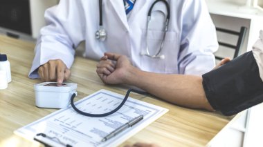 Erkek doktor, check-up, tıbbi tedavi ve sağlık konsepti için hastaneye gelen hastaların vücut basıncını ve nabzını ölçmek için kan basıncı monitörü kullanır..