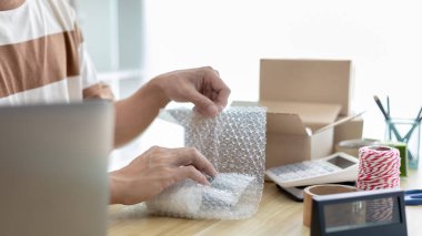 Adam posta kutusunu paketleyip müşteriye teslim etmeye hazırlanıyor, evde çalışıyor ve işletme sahibi oluyor, çevrimiçi alışveriş KOBİ girişimcisi, paketleme kutusu, çevrimiçi satış, serbest çalışma.