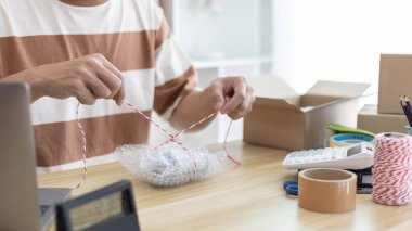 Adam posta kutusunu paketleyip müşteriye teslim etmeye hazırlanıyor, evde çalışıyor ve işletme sahibi oluyor, çevrimiçi alışveriş KOBİ girişimcisi, paketleme kutusu, çevrimiçi satış, serbest çalışma.