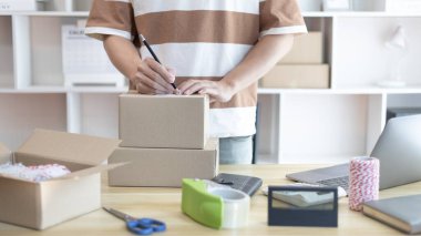 Genç Asyalı müşteri bilgilerini ve adreslerini not defterine ya da kutuya yazarak bilgilere göre nakliyeye hazırlanıyor. Paketleme kutusu, çevrimiçi satış, serbest çalışma..