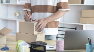 Genç Asyalı müşteri bilgilerini ve adreslerini not defterine ya da kutuya yazarak bilgilere göre nakliyeye hazırlanıyor. Paketleme kutusu, çevrimiçi satış, serbest çalışma..