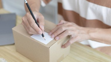 Genç Asyalı müşteri bilgilerini ve adreslerini not defterine ya da kutuya yazarak bilgilere göre nakliyeye hazırlanıyor. Paketleme kutusu, çevrimiçi satış, serbest çalışma..