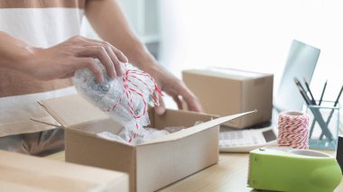 Adam posta kutusunu paketleyip müşteriye teslim etmeye hazırlanıyor, evde çalışıyor ve işletme sahibi oluyor, çevrimiçi alışveriş KOBİ girişimcisi, paketleme kutusu, çevrimiçi satış, serbest çalışma.