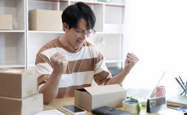 Bir internet müşterisinden sipariş aldıktan sonra mutlu olan adam, evde çalışan ve iş sahibi gençler için yeni bir iş tarzı, online alışveriş KOBİ girişimcisi, paketleme kutusu, çevrimiçi satış.