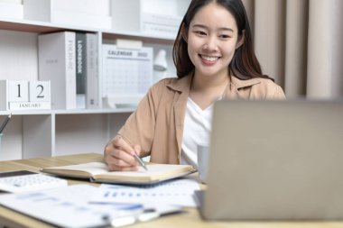 Not defterine not alan Asyalı kadın evde dizüstü bilgisayarda çalışırken, görüntülü sohbet, online iletişim, Evde kal, Yeni Normal, Mesafeli Öğrenme