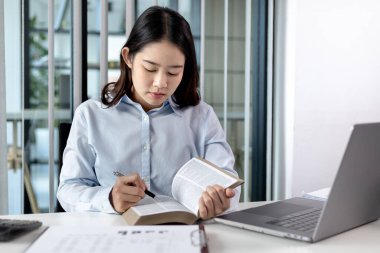 Özel bir ofiste kitap okuyan genç bir kız öğrenci, şehirlerarası eğitim, kitaplardan ders kitapları, daha fazla bilgi edinin, ofiste masanın üzerine yerleştirilmiş bir bilgisayar ya da dizüstü bilgisayar var,.