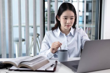 İş kadını laptopta çalışıyor, kahvesini rahatça yudumluyor, özel bir ofiste oturuyor, finansal işlemleri yürütmek için bilgisayarları kullanıyor, teknoloji ve internet dünyası, iş hayatı....