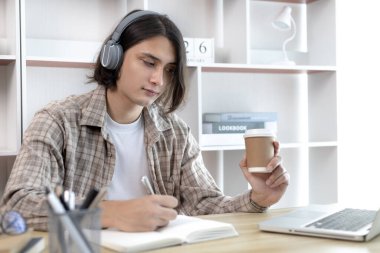 Asyalı adam evde dizüstü bilgisayarda çalışırken not alıyor, görüntülü sohbet, online iletişim, Evde kal, Yeni Normal, Mesafe Öğrenme, Sosyal Mesafe Öğrenme, Çevrimiçi Öğrenme.