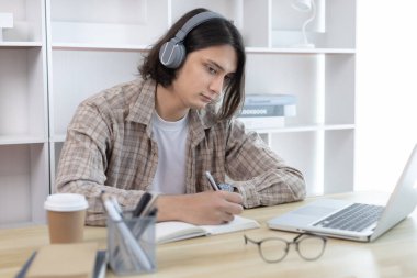 Asyalı adam evde dizüstü bilgisayarda çalışırken not alıyor, görüntülü sohbet, online iletişim, Evde kal, Yeni Normal, Mesafe Öğrenme, Sosyal Mesafe Öğrenme, Çevrimiçi Öğrenme.