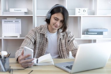 Genç öğrenci ödevini yapıyor ve sömestr tatilinde laptopunda canlı olarak yayınlanıyor, Evde kal, Yeni Normal, Mesafe Öğrenme, Sosyal Mesafe Öğrenme, Çevrimiçi, Şehirlerarası İletişim.